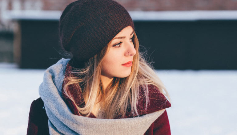 young blonde woman wearing beanie and scarf, standing outside in winter