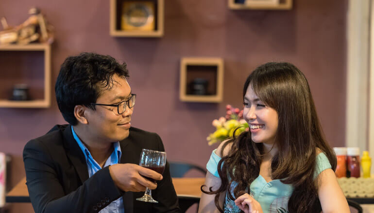 man with glasses sitting at restaurant counter with brunette woman, smiling at each other