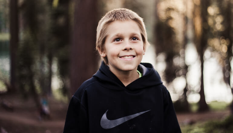 Blonde young boy wearing a black Nike sweatshirt in the foods smiles because he maintains great oral hygiene