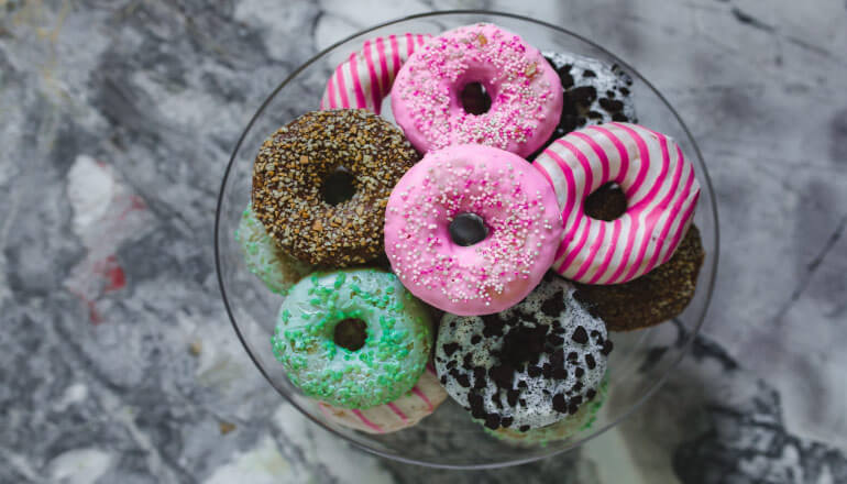 Aerial view of a plate of donuts with pink, brown, green, and white icing with lots of sugar