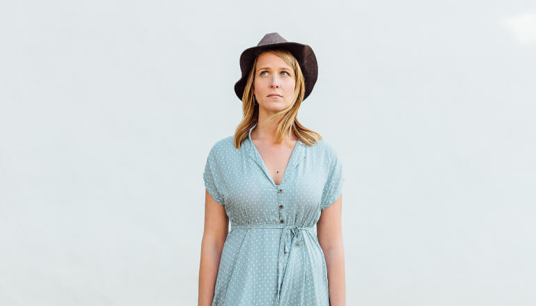 Blonde woman wearing a blue dress and hat wonders which diseases affect oral health