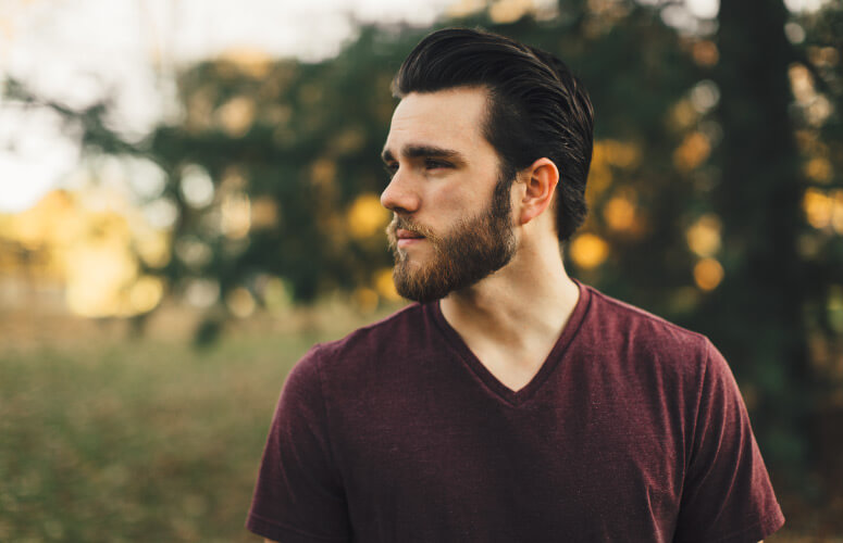 Brunette man with a beard wears a maroon V-neck shirt outside while thinking about cavities