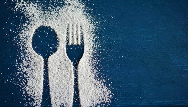 A silhouette of a fork and spoon in powdered sugar on a blue counter