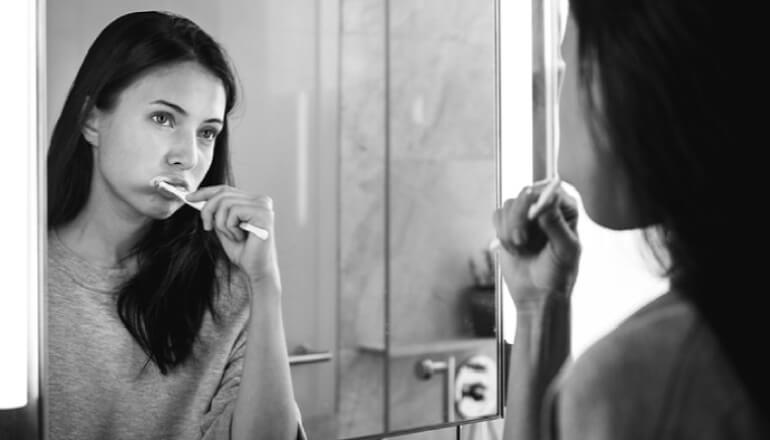 girl looking in the mirror brushing her teeth to avoid tooth decay and cavities