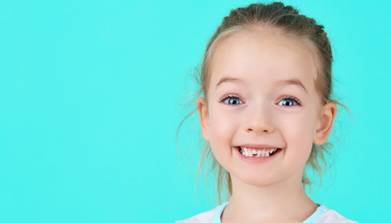 Smiling girl on a bright mint colored background with a missing baby tooth on the bottom