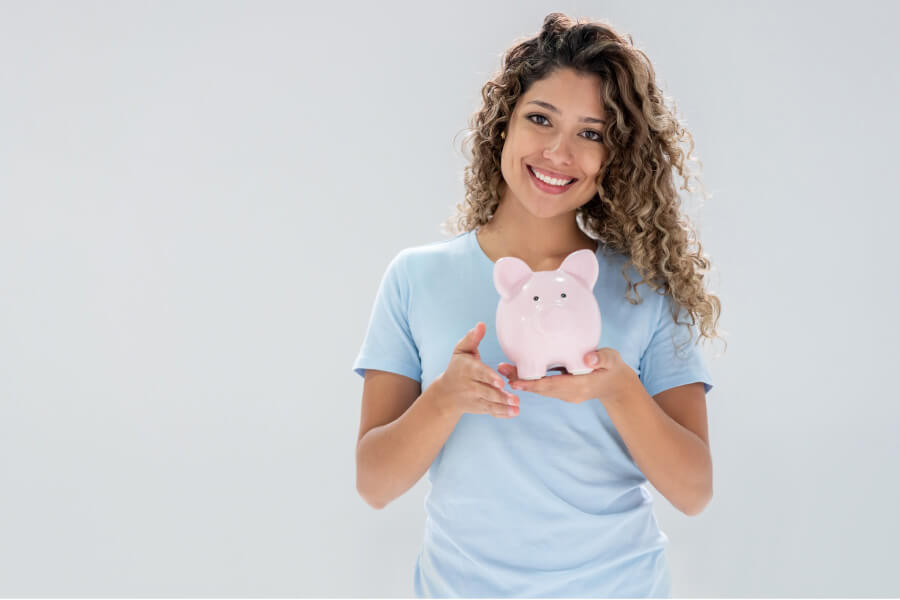 young woman holds a pink piggybank and smiles because of affordable dentistry