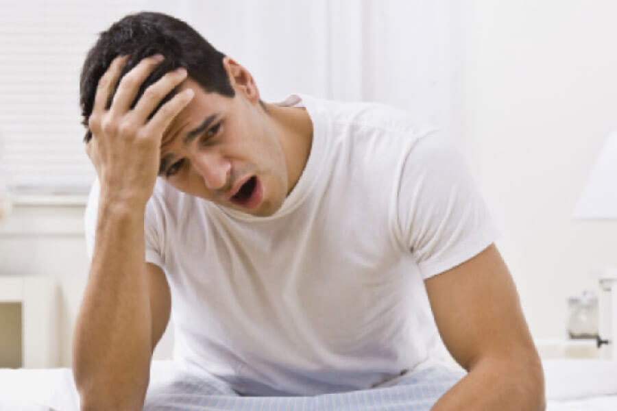 man wakes up holding his head and yawning after a night of teeth grinding