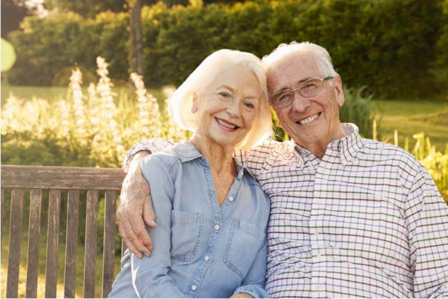 senior couple sitting on a bench hug and smile after learning about dentures