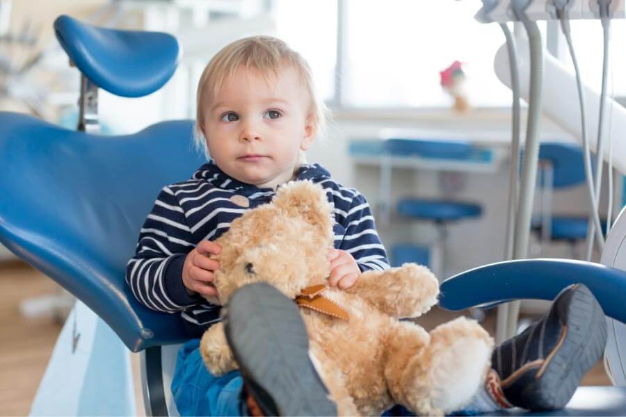 young boy holding a teddy bear sits in the dentist's chair