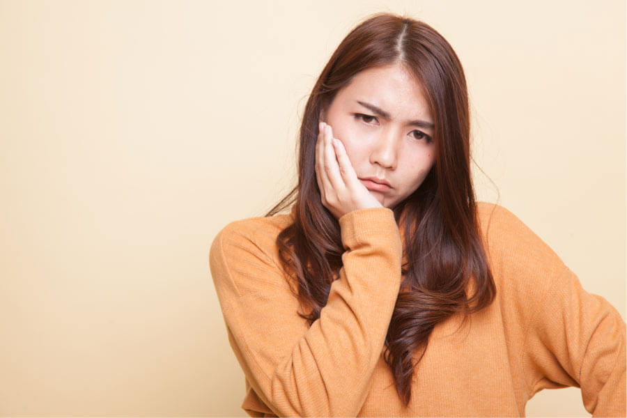 teen girl holds her jaw in pain from emerging wisdom teeth