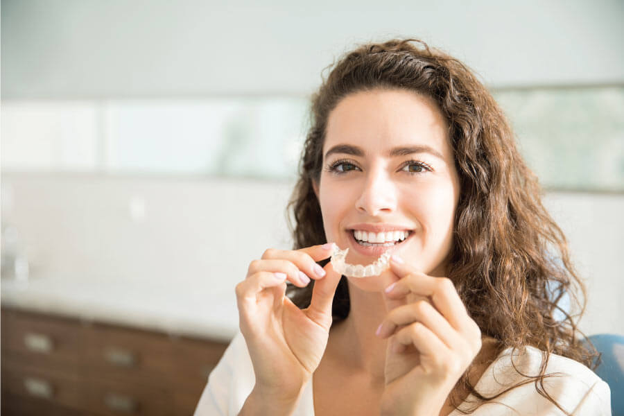 woman smiles and hold up her clear aligner