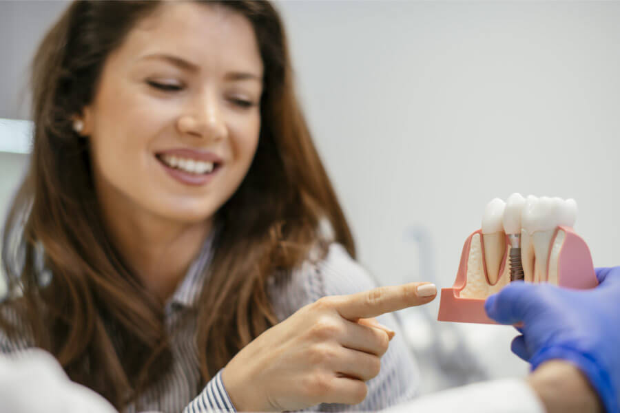 young woman points to a dental implant model while learning about the process