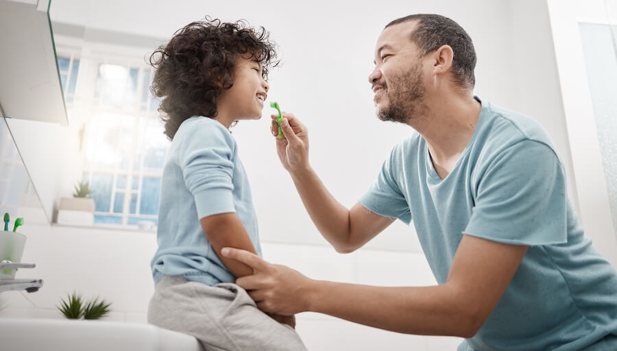 parent with son brushing his teeth to teach kids dental habits