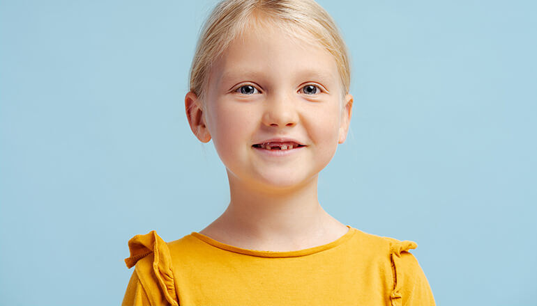 Smiling girl on a bright mint colored background with a missing baby tooth on the bottom